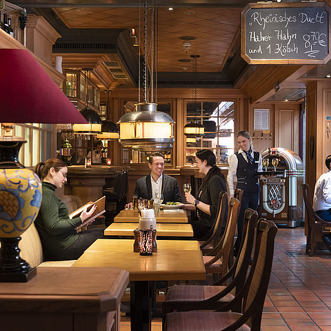 Clienti alla taverna "Kölsche Stuff" gustano cibo in un'atmosfera accogliente e rustica.