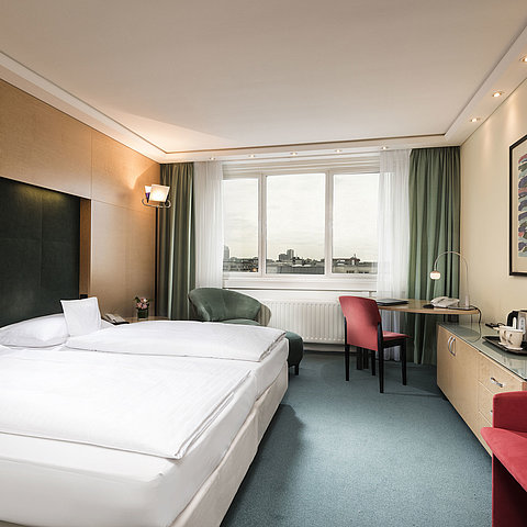 Camera Comfort al Maritim proArte Hotel Berlin con letto matrimoniale, scrivania, poltrona e vista sulla città.