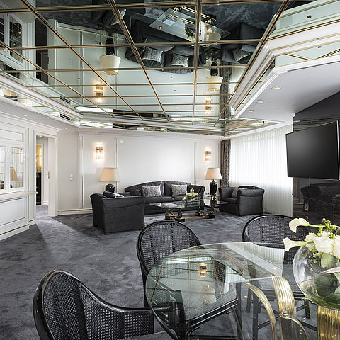 Soggiorno elegante della suite di lusso dell'Hotel Maritim con soffitto a specchio, mobili moderni e grande tavolo da pranzo.