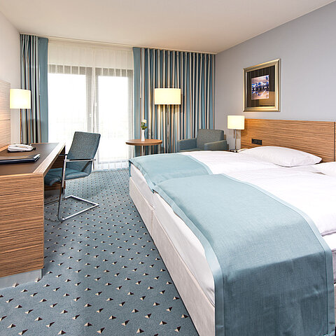 Camera comfort al Maritim Hotel Darmstadt con design moderno, scrivania, area salotto accogliente e ampie finestre.