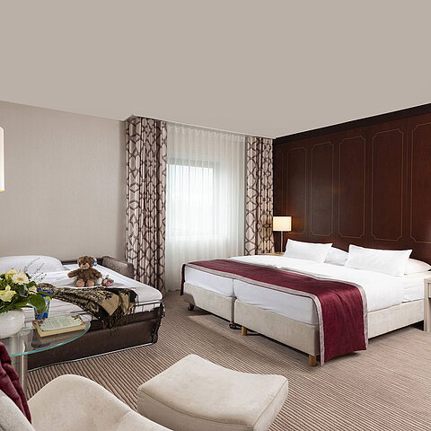 Camera familiare Comfort al Maritim Hotel Bonn con letto matrimoniale, divano letto, poltrona e composizione floreale.