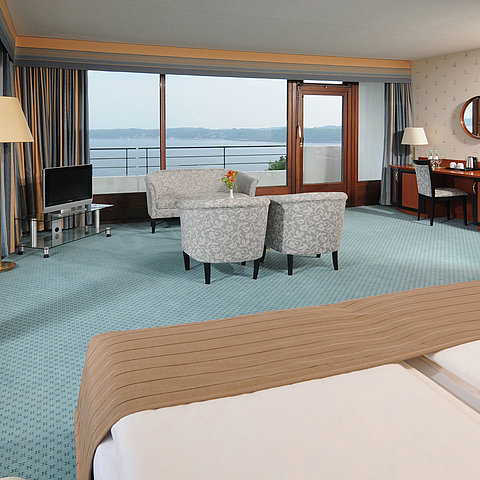 Junior Suite del Maritim Hotel Kiel, con area salotto, scrivania, TV e ampia finestra frontale con vista sul mare.
