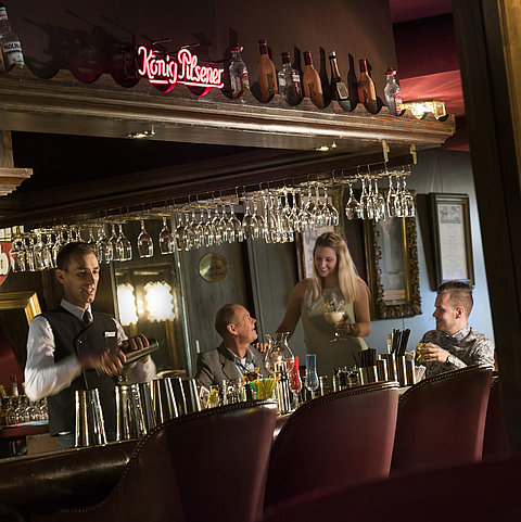 Atmosfera del bar del Maritim Hotel Kiel con gli ospiti che gustano un cocktail mentre il barista prepara un drink.