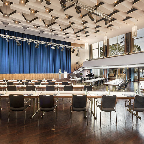 Grande salle « Maritim » au Maritim Seehotel Timmendorfer Strand avec scène, rideaux bleus et sièges pour conférences.