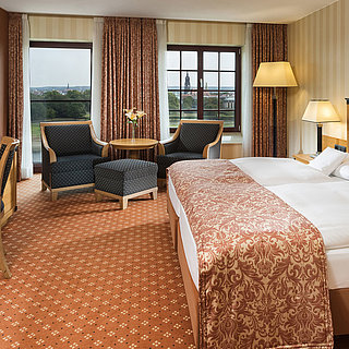 Chambre supérieure à l'hôtel Maritim de Dresde avec lit double élégant, bureau et coin salon avec vue sur la ville.
