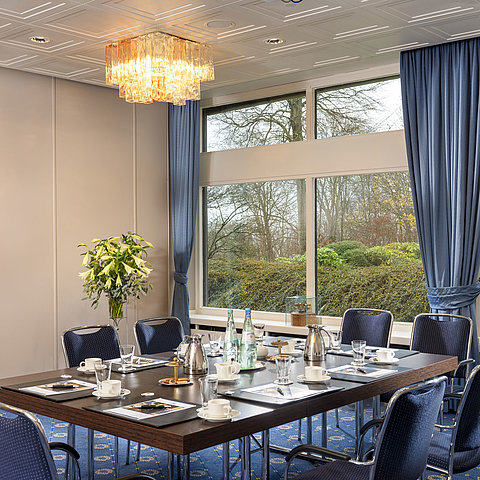 Salon Flensburg à l'hôtel Maritim de Kiel, salle de conférence avec table dressée, grandes fenêtres et éclairage stylé.