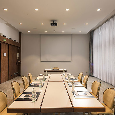 Salle de conférence « Salon Bonn » au Maritim Seehotel Timmendorfer Strand avec table de réunion, lumière naturelle et écran.