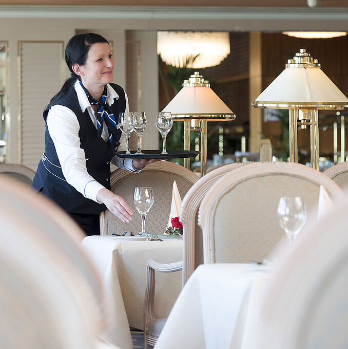 Serveuse dresse une table au restaurant de l'hôtel Maritim Timmendorfer Strand, avec une ambiance élégante et des lampes en verre.