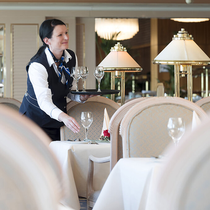 Cameriera apparecchia un tavolo nel ristorante dell'Hotel Maritim Timmendorfer Strand, con un'atmosfera elegante e lampade in vetro.