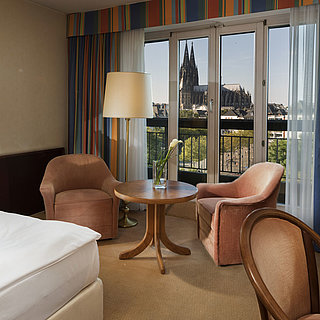 Chambre supérieure à l'hôtel Maritim Cologne avec coin salon, lit confortable et vue sur la cathédrale de Cologne.