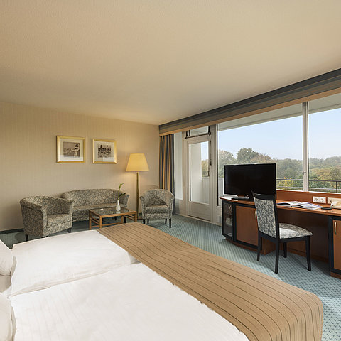 Camera comfort del Maritim Hotel Kiel con accogliente area salotto, scrivania, ampio letto e splendida vista sulla campagna.