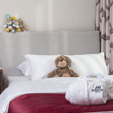 Suite familiare al Maritim Hotel Bonn con letto accogliente, peluche e accappatoio, perfetto per i bambini.