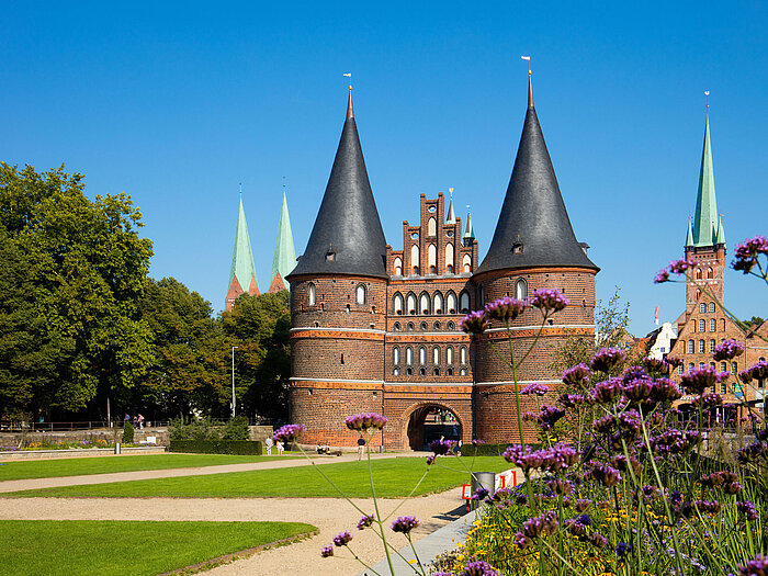 La porte de Holstein à Lübeck avec des fleurs en pleine floraison et un ciel bleu.