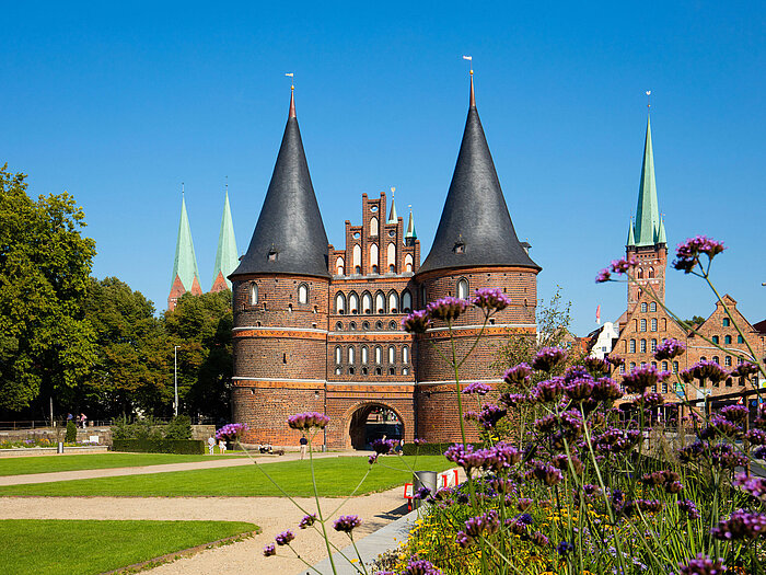 Holstentor a Lubecca con fiori in fiore in primo piano e cielo azzurro.