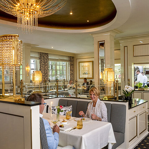Coppia che gode una cena raffinata al ristorante Orangerie del Maritim Seehotel Timmendorfer Strand con vista sulla cucina.