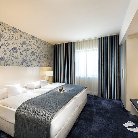 Suite elegante presso il Maritim Hotel Bonn con un grande letto, copriletto blu e arredi eleganti.