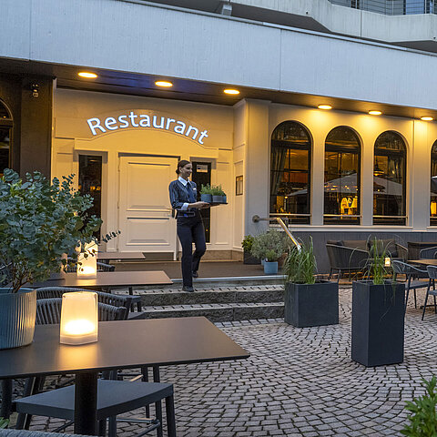 Evening atmosphere on the terrace of the Maritim Hotel Darmstadt with a staff member carrying a tray to the restaurant.