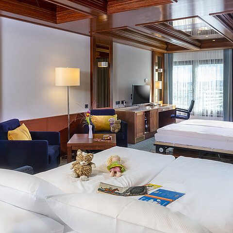 Camera familiare al Maritim Hotel Darmstadt con giocattoli sul letto, scrivania con TV e area salotto accogliente.