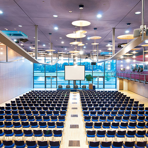 Grande salle de conférence de l'hôtel Maritim de Dresde avec des rangées de chaises bleues et vue sur l'Elbe.