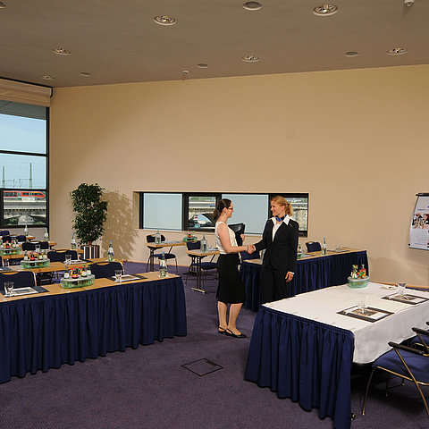Salle de réunion lumineuse de l'hôtel Maritim de Dresde avec tables dressées, tableau et deux personnes se serrant la main.