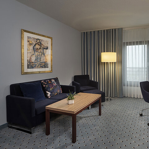 Junior suite al Maritim Hotel Darmstadt con arredi eleganti, divano, scrivania, TV e grandi finestre per molta luce naturale.