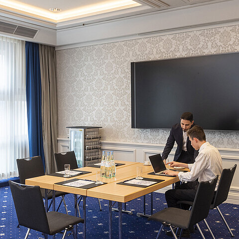 Deux personnes travaillant dans le Salon Oegg de l'hôtel Maritim Würzburg avec un écran moderne.