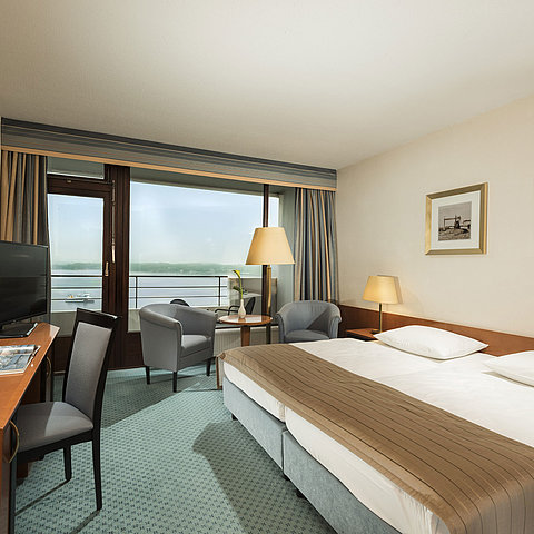 Camera superior del Maritim Hotel Kiel con scrivania, area salotto, ampio letto matrimoniale e balcone con vista sul fiordo.