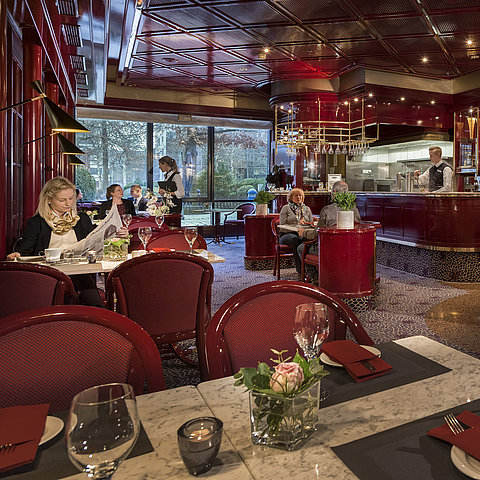 L'immagine mostra il caffè accogliente "Brasserie" presso il Maritim Hotel Bonn con decorazioni rosse e un'atmosfera rilassata.