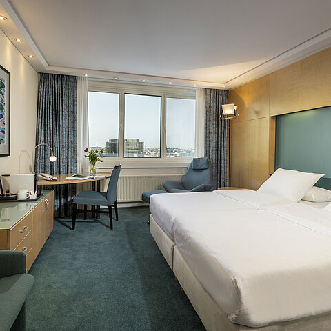 Camera Superior arredata in stile moderno presso l'hotel Maritim con letto grande,scrivania, opera d'arte e vista sulla città