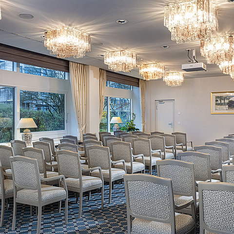 Salon Helsinki à l'hôtel Maritim de Kiel, salle de conférence avec des rangées de chaises, des lustres et de grandes fenêtres avec vue sur la verdure.