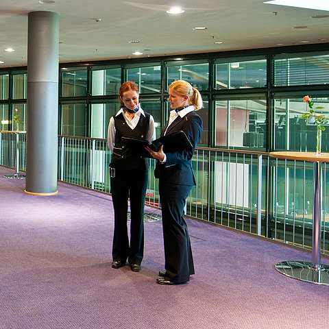 Foyer de l'hôtel Maritim de Dresde avec deux employés en uniforme, des tables hautes et un buffet de fruits.