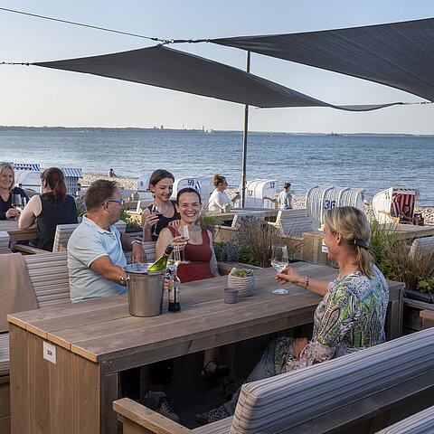 Gruppo di ospiti al bar sulla spiaggia del Maritim Seehotel Timmendorfer Strand che beve con vista mare e sdraio.