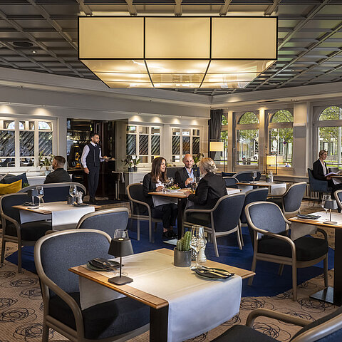 Ristorante elegante del Maritim Darmstadt con ospiti che cenano e si rilassano. Arredi moderni e grandi finestre con vista.