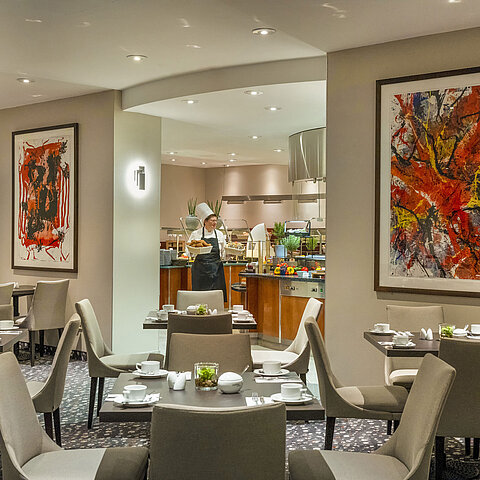 Ristorante del Maritim proArte Hotel Berlin con arte moderna alle pareti, tavoli apparecchiati e uno chef al buffet.