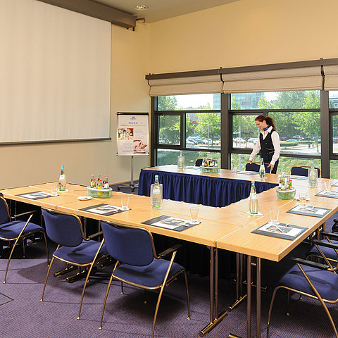 Salle de réunion de l'hôtel Maritim de Dresde avec tables en U, écran de présentation et préparations pour une réunion.