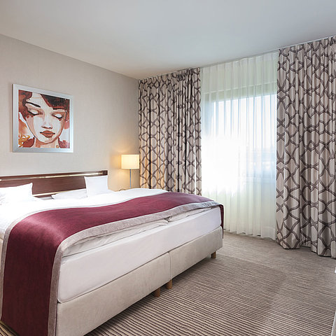 Ampia suite presso il Maritim Hotel Bonn con letto matrimoniale accogliente, arredamento moderno e copriletto rosso vino.