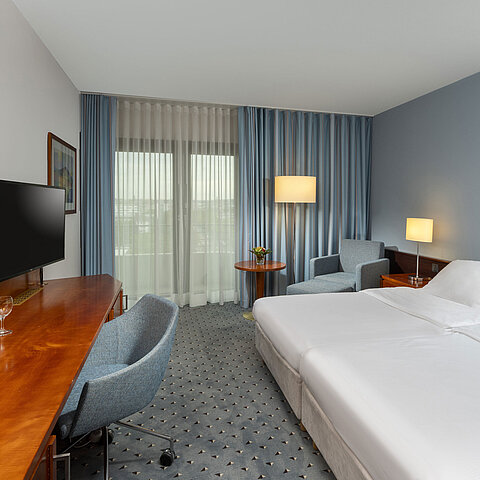 Camera doppia classica al Maritim Hotel Darmstadt con scrivania, TV a schermo piatto,area salotto e grandi finestre con tende